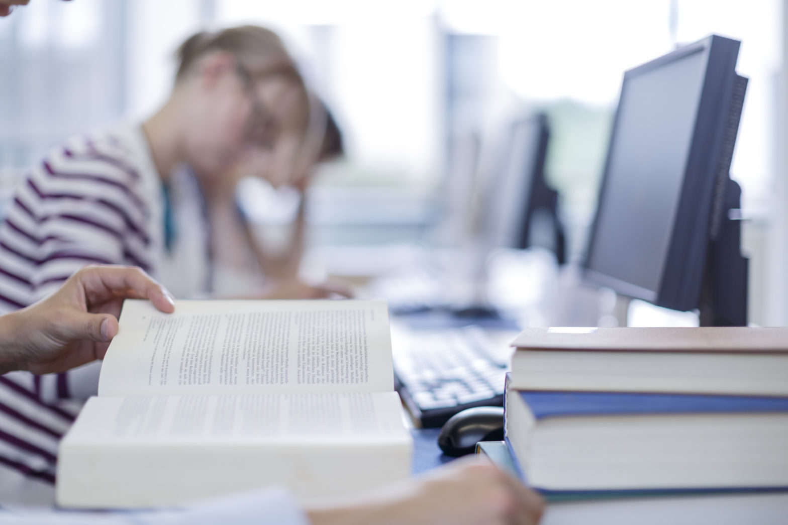 Studenten lernen vor Büchern und Computern, der Fokus liegt auf den Büchern im Vordergrund